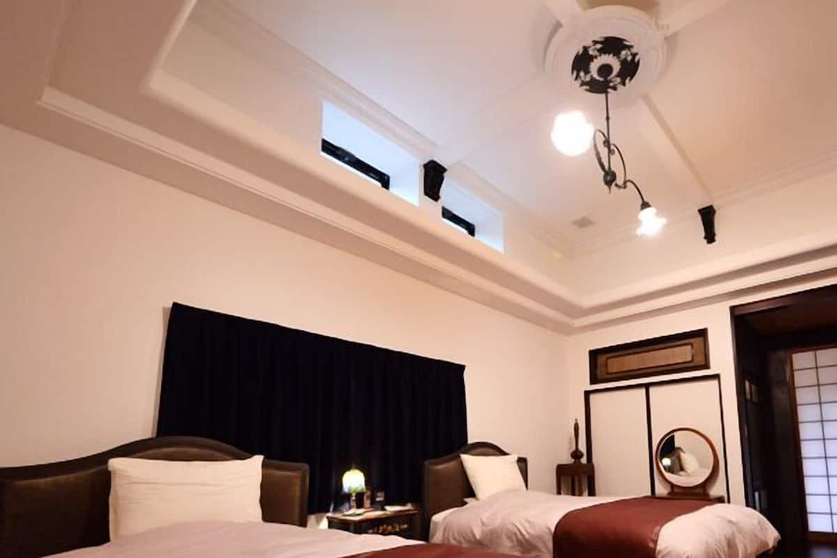 A hotel room with two beds, a ceiling fan, a nightstand with a lamp, and a window.