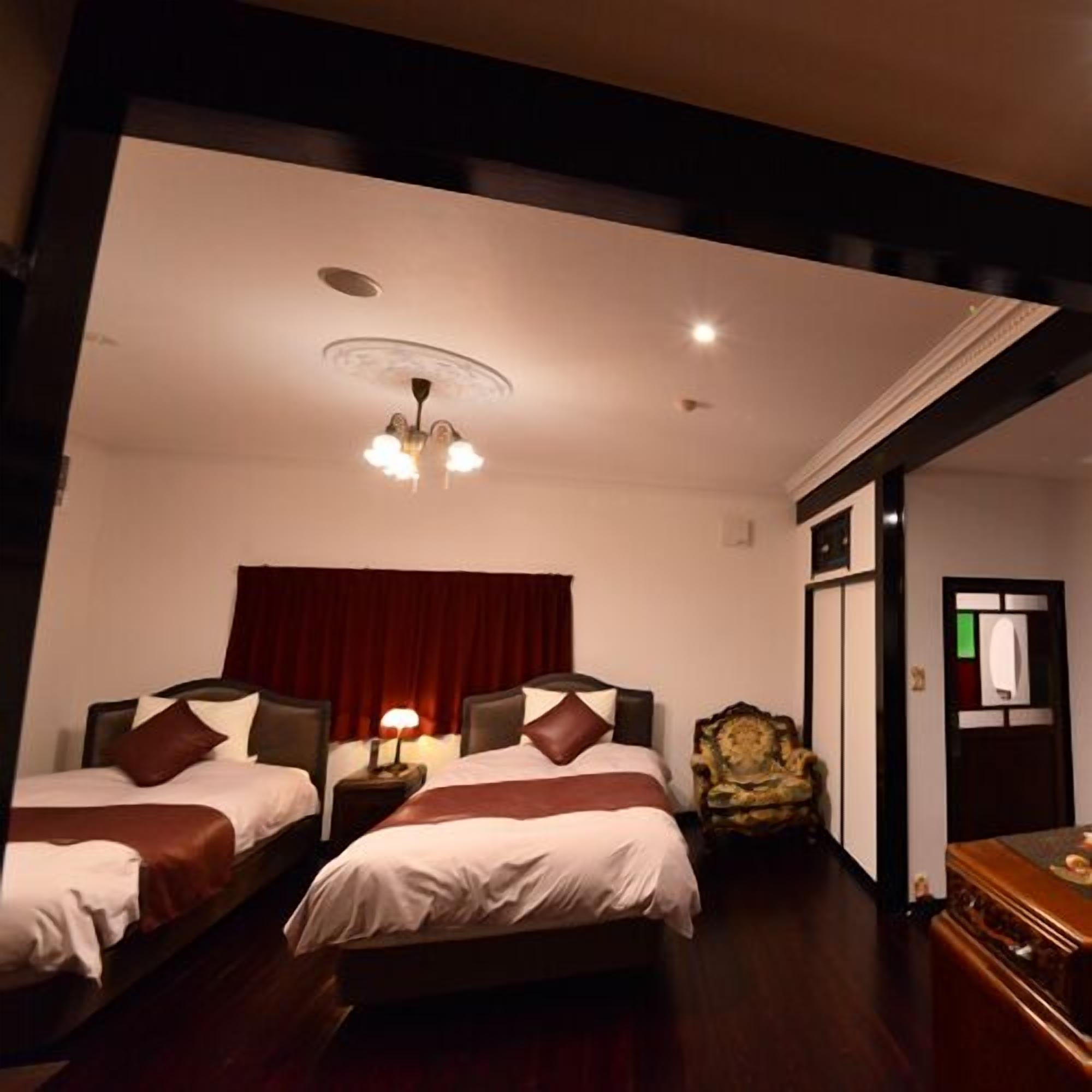 A hotel room with two beds, a chandelier, a wooden dresser, and a red curtain.