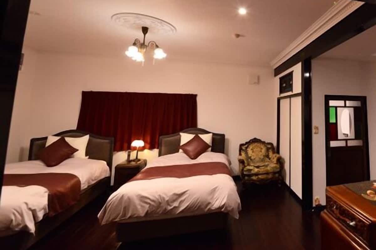 A hotel room with two beds, a chandelier, a wooden dresser, and a red curtain.