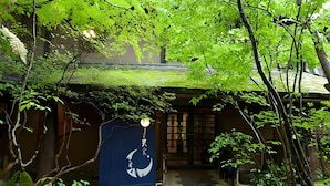Un jardin japonais traditionnel, avec un sentier menant à un bâtiment sur lequel est apposée une enseigne bleu foncé représentant une lune et des étoiles.