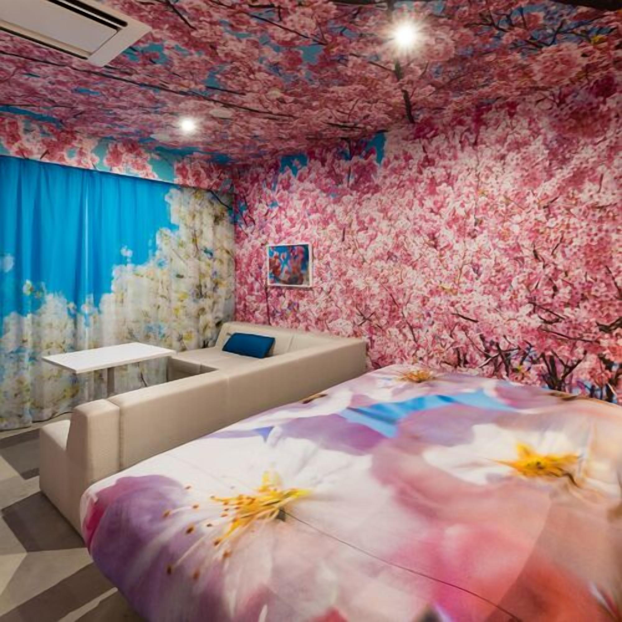 A room with a floral ceiling, a bed with a floral bedspread, a sofa, a small table, and a picture on the wall.