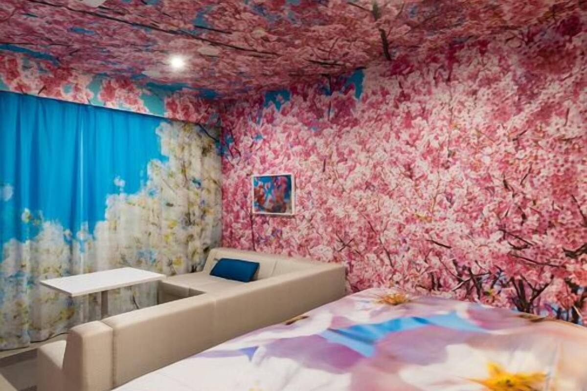 Una habitación con techo floral, una cama con cubrecama floral, un sofá, una mesita y un cuadro en la pared.