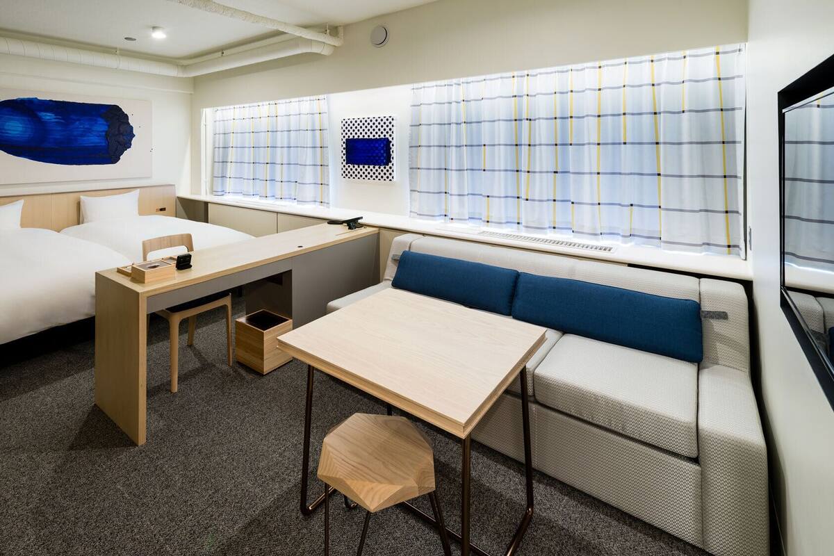 Una habitación de hotel moderna con cama, escritorio, zona de estar y ventanas amplias.