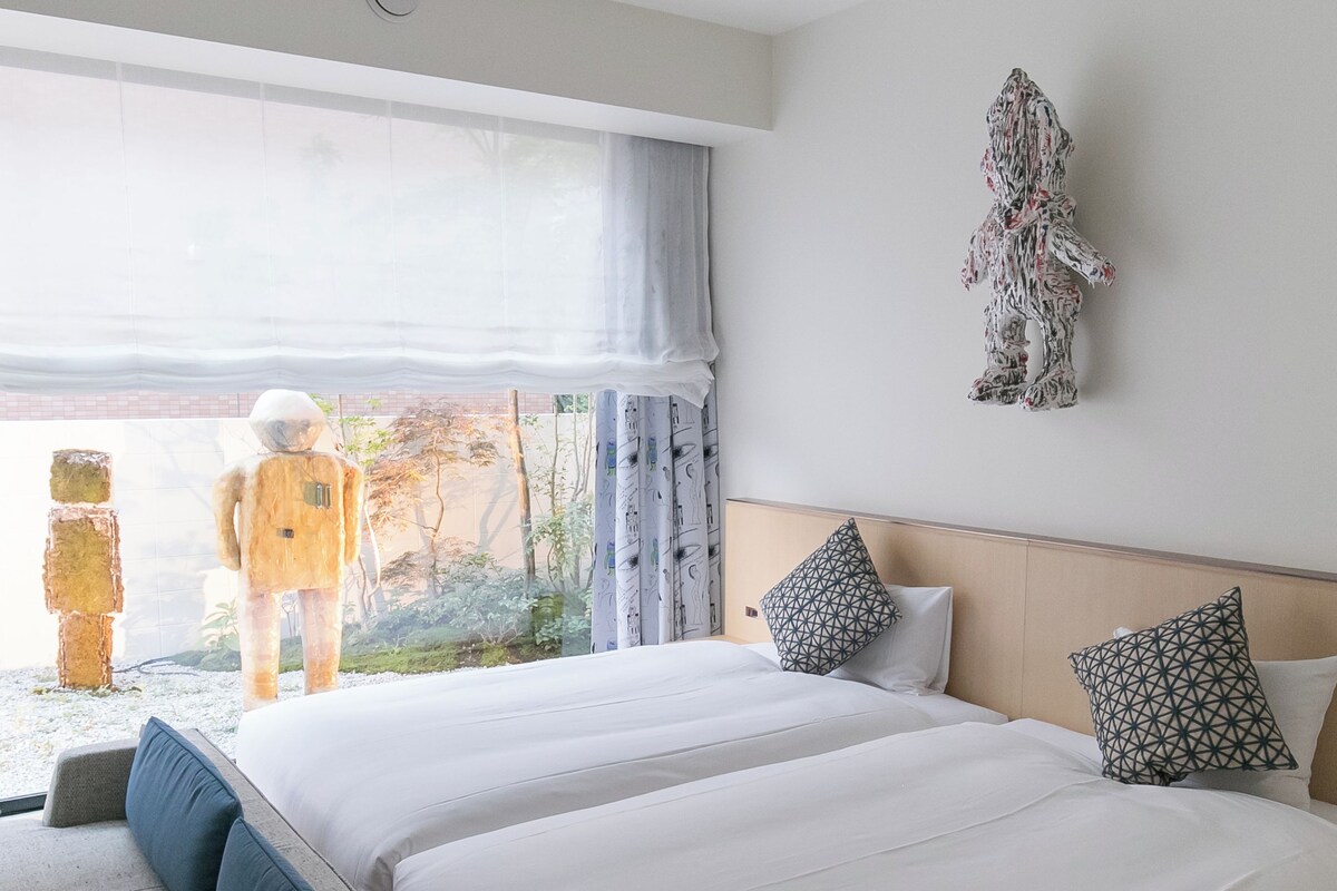 A hotel room with a large bed, a sofa, a view of the outdoors, and a wall decoration.