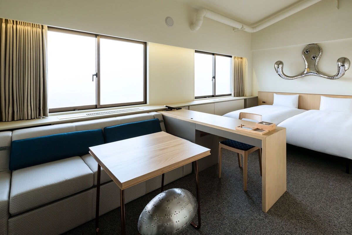 Una habitación de hotel con una cama, un escritorio, una silla, un sofá y una ventana.
