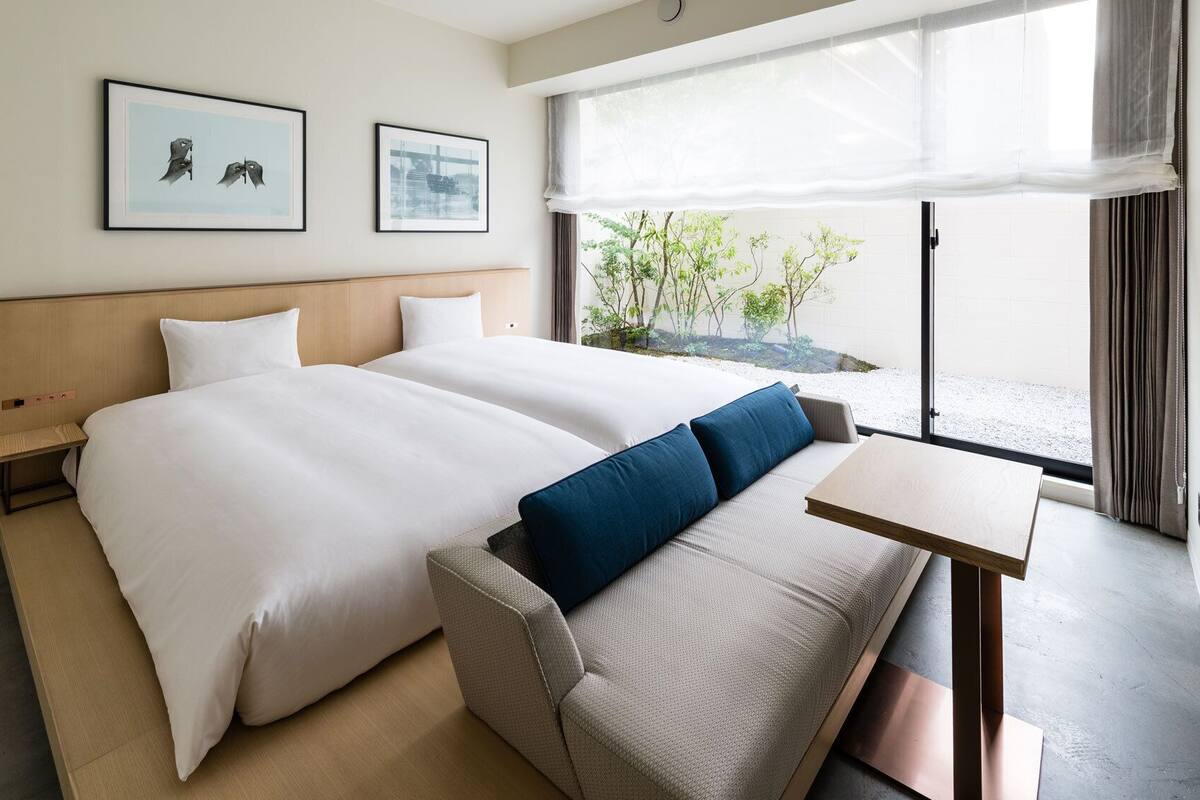 Habitación de hotel con dos camas, una mesita, un sofá y vistas a zonas verdes.