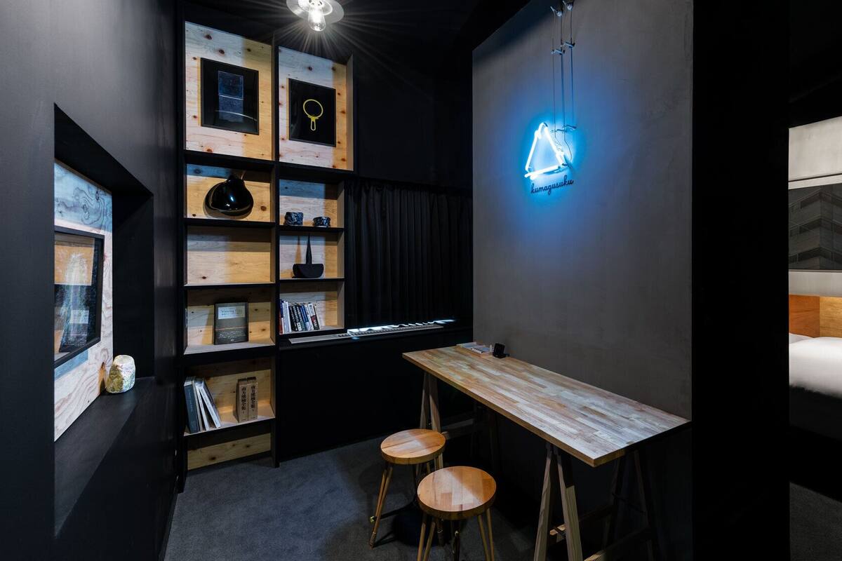 Una habitación de hotel moderna con un escritorio de madera, dos taburetes, una estantería y un letrero de neón.