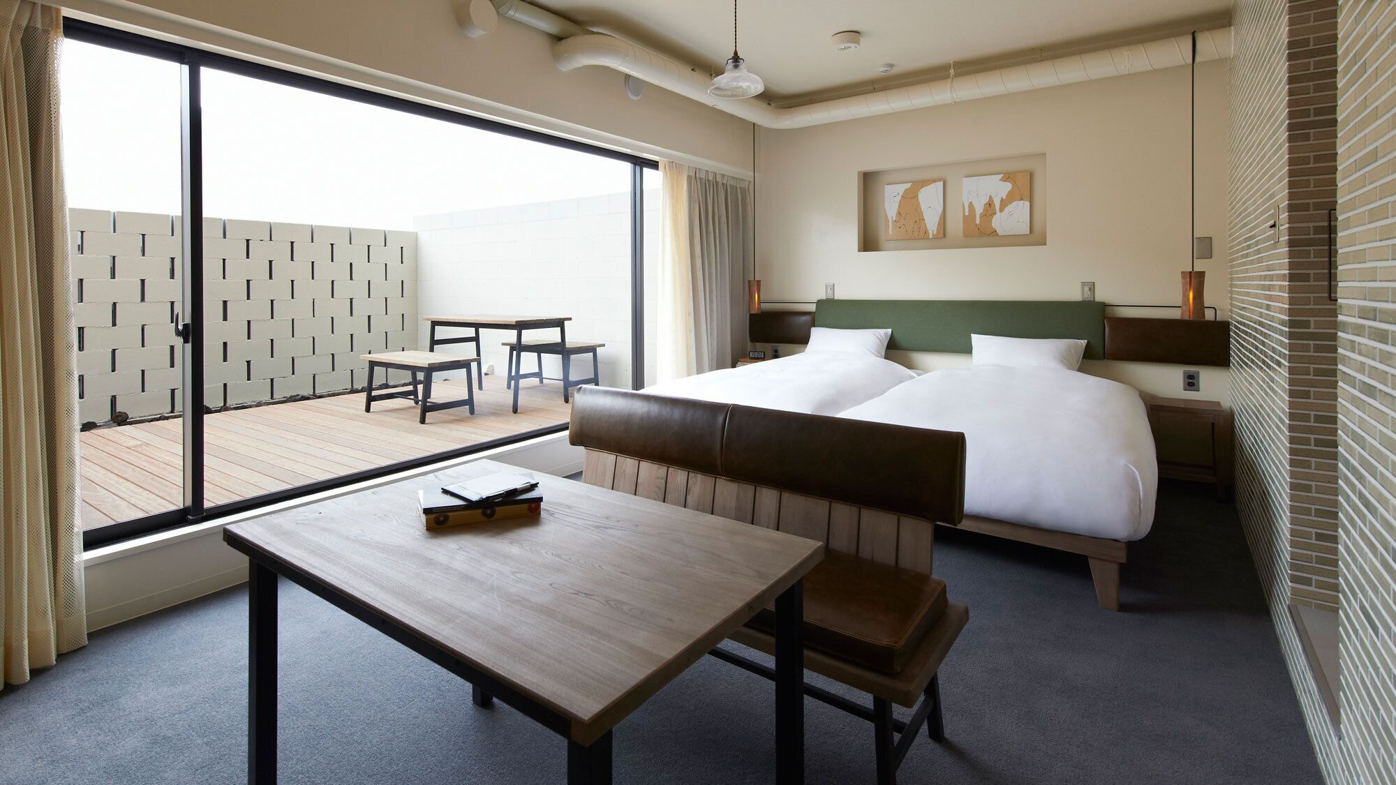 A hotel room with a bed, a desk, a chair, a table, a balcony with a view, and artwork on the wall.