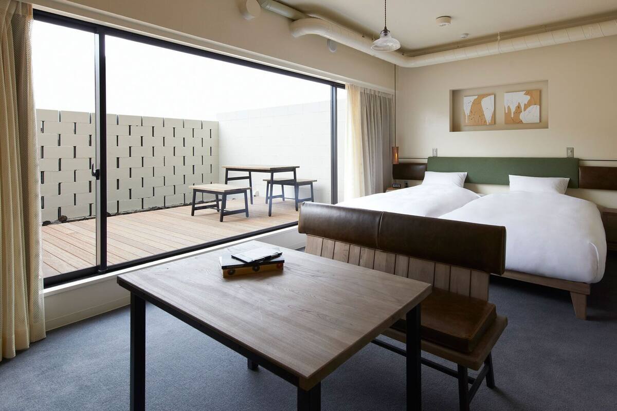 Habitación de hotel con cama, escritorio, silla, mesa, balcón con vistas y obras de arte en la pared.
