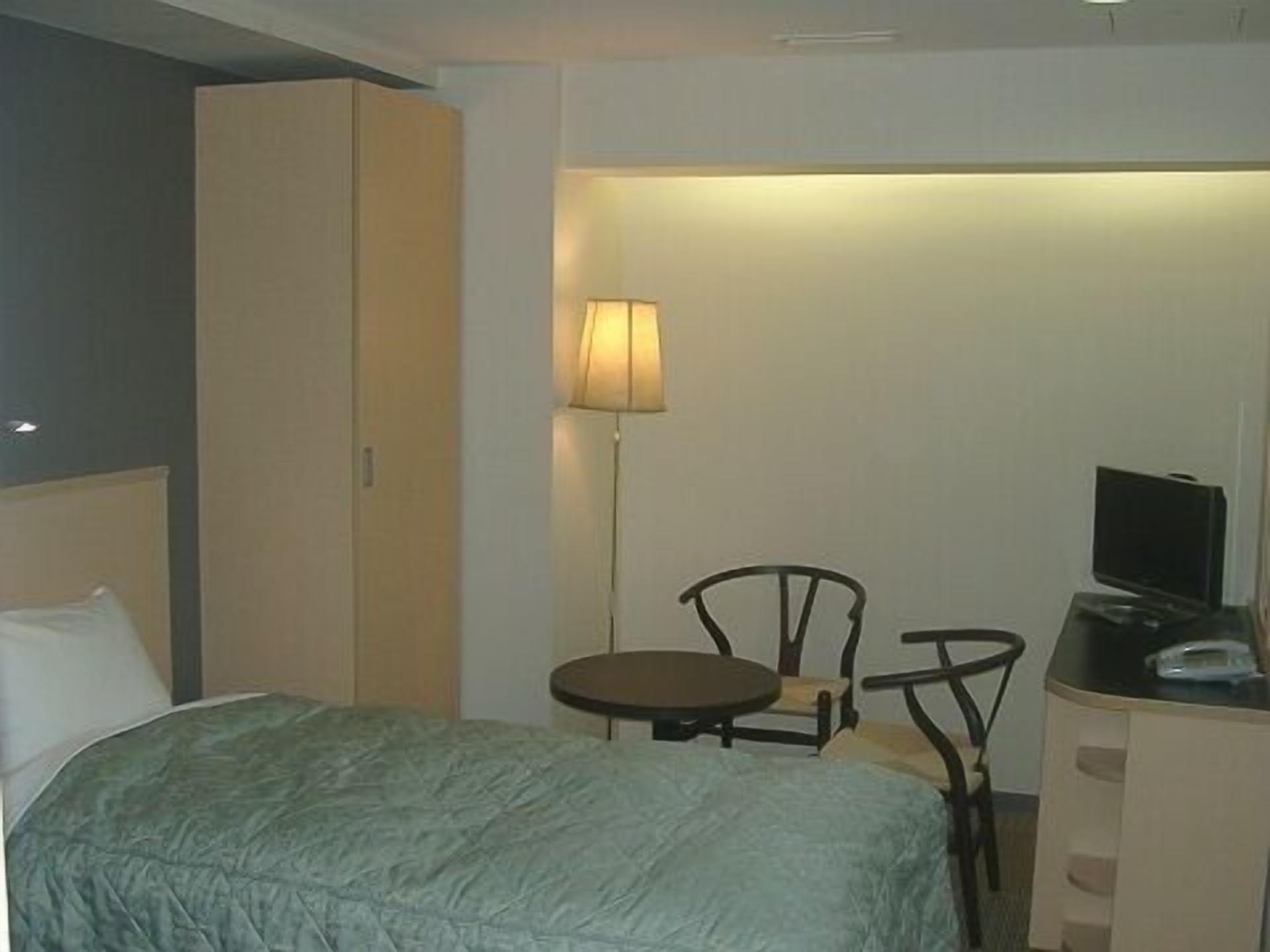 Ein Hotelzimmer mit einem Bett, einem Schreibtisch mit Fernseher, einem Sessel und einer Lampe.