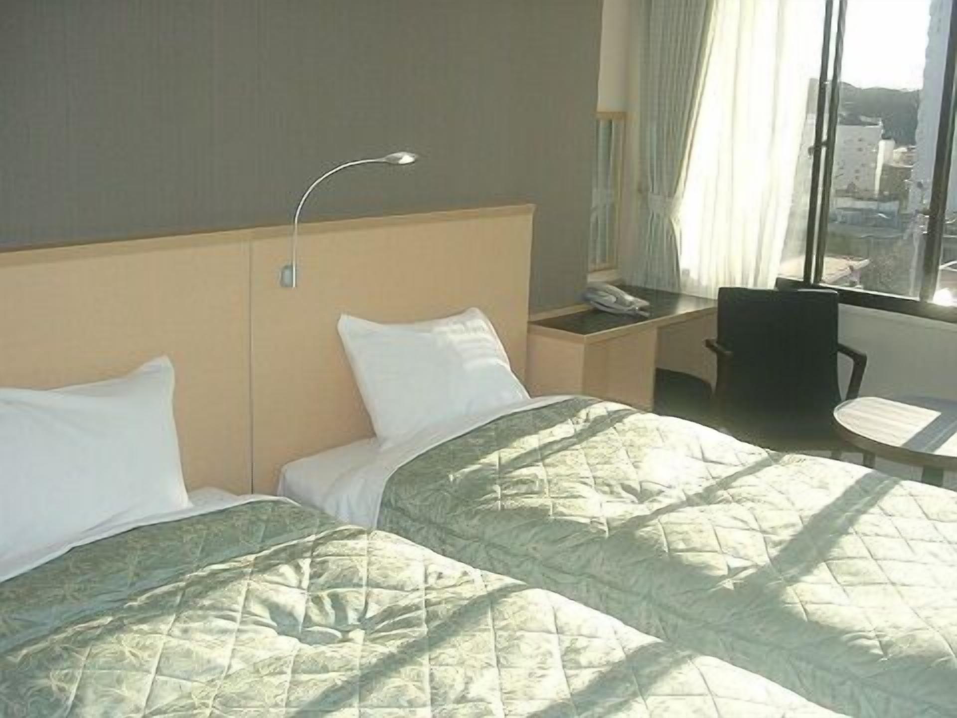 Habitación de hotel con dos camas, un escritorio con teléfono, una silla y una ventana con vista a edificios.