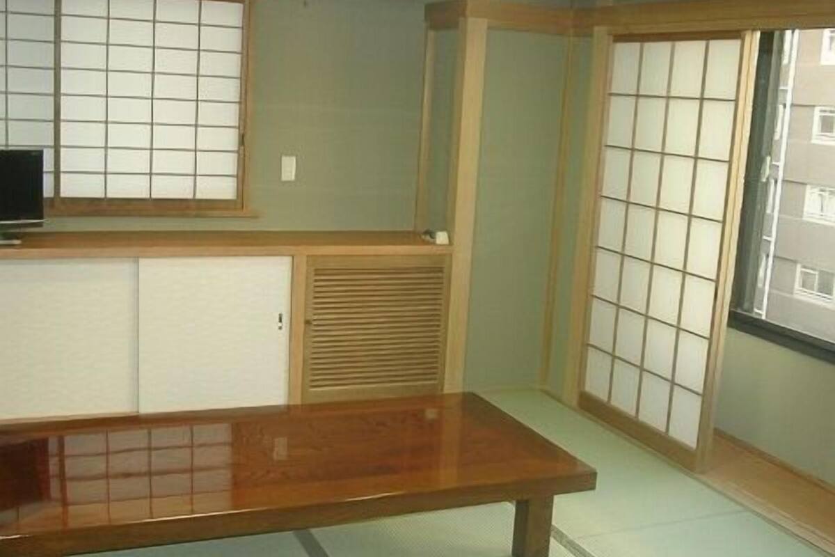 A traditional Japanese room with tatami flooring, a low wooden table, sliding doors, and a television on a low shelf.
