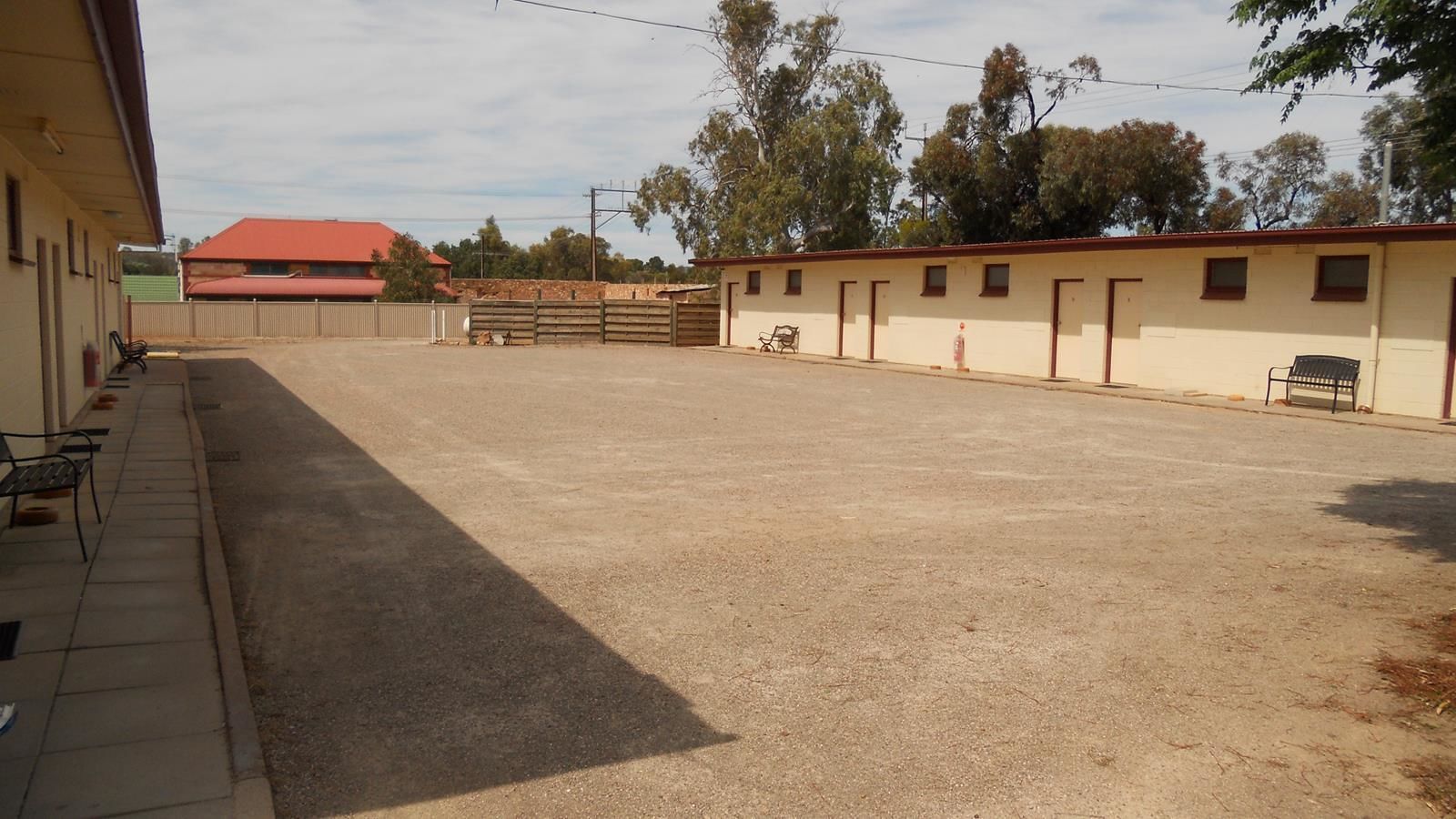 A spacious indoor area with a dirt floor, benches along the walls, and a fence in the background.