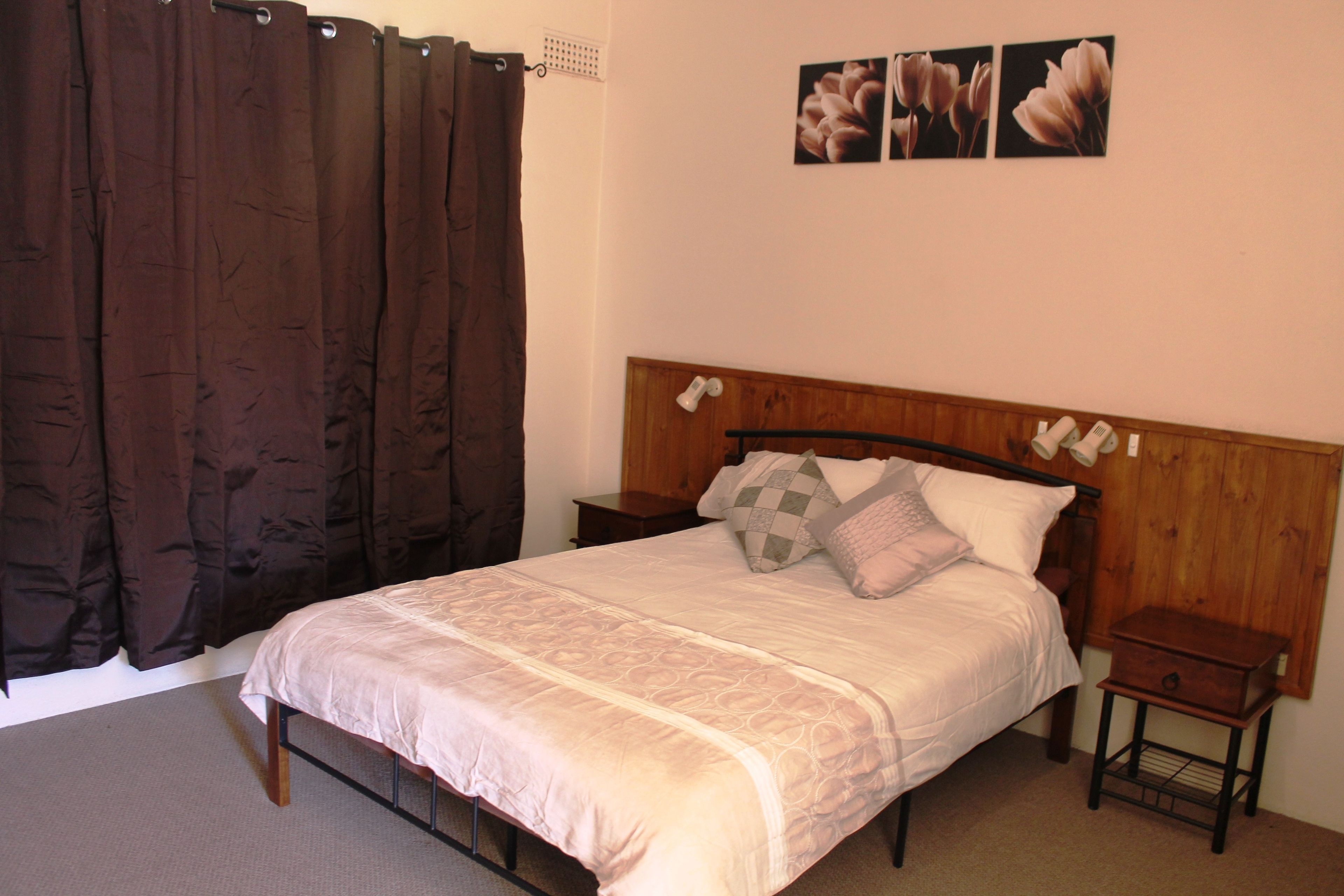 A bedroom with a bed, wooden headboard, two bedside tables, a nightstand, and a curtain.