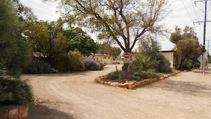 A gravel driveway leading to a building with a 'No Entry' sign, surrounded by landscaped gardens and trees. - Flinders Ranges Motel (Quorn)