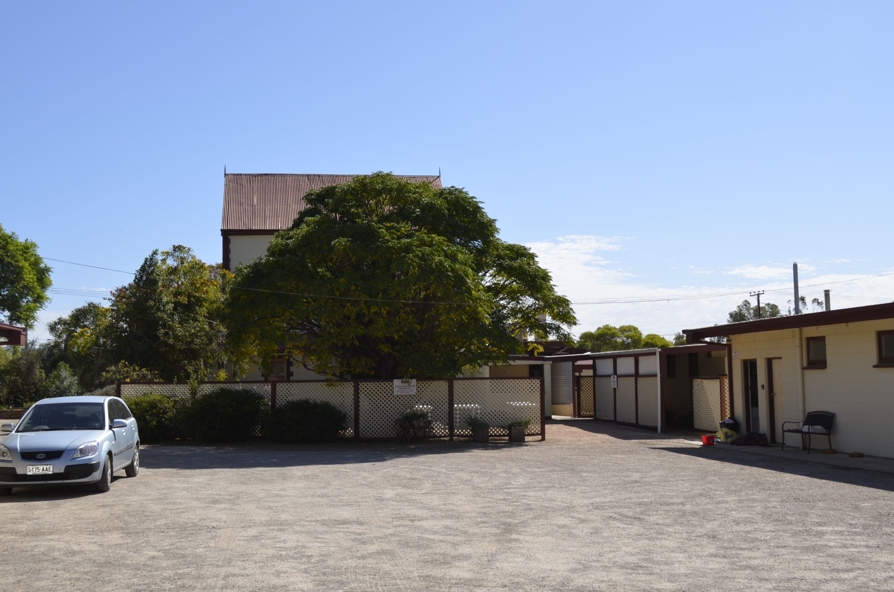 A parking lot with a building in the background, a tree, and a car.