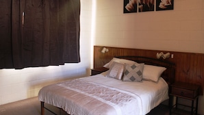 A bedroom with a wooden headboard, a bed with a white bedspread, two nightstands, and a window with dark curtains. - Flinders Ranges Motel (Quorn)