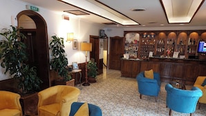 Eine Lobby mit Barbereich, verschiedenen Sitzgelegenheiten, darunter gelbe und blaue Sessel, und einem gemusterten Boden.