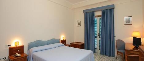 Une chambre d’hôtel avec un grand lit, des tables de chevet avec des lampes, un bureau avec une chaise et une fenêtre avec des rideaux.