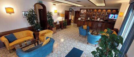 A lobby with a bar area, sofas, and potted plants.