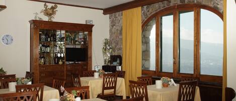 Un área de comedor con mesas y sillas, una barra con botellas, y un ventanal con vistas.