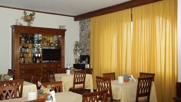 Un comedor con mesas y sillas de madera, una alacena bar con botellas y un televisor.
