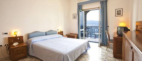 A hotel room with a bed, nightstands, a TV, and a balcony with a view.