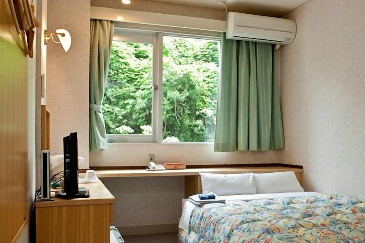 A compact hotel room with a bed, desk, and window.