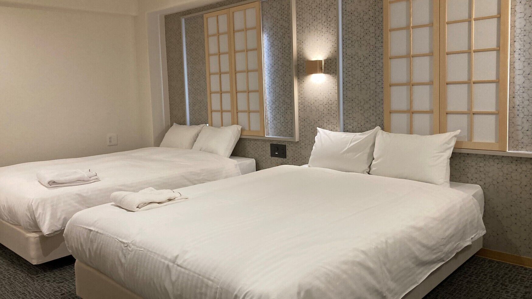 A hotel room with two beds, a wall-mounted light, and a window with a view.