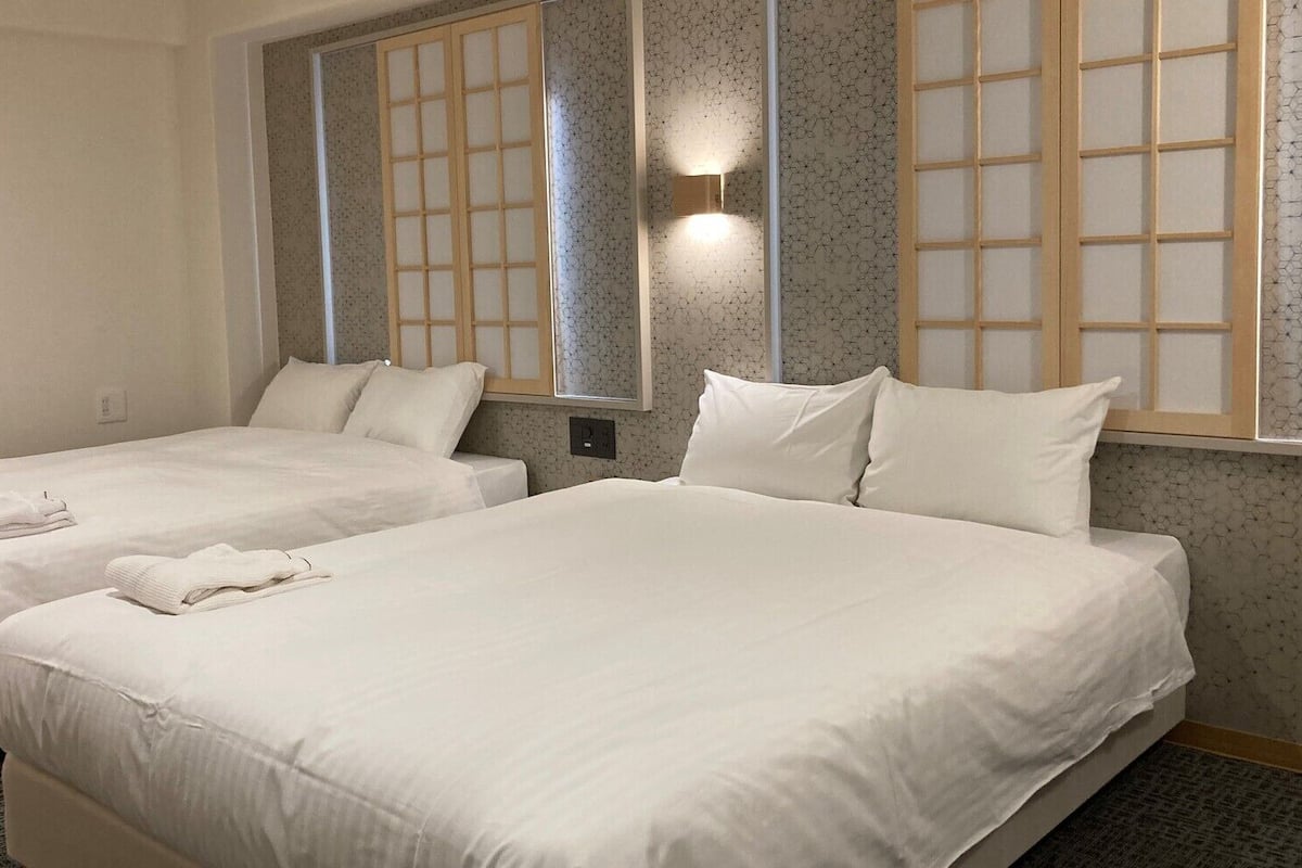 Habitación de hotel con dos camas, una lámpara de pared y una ventana con vistas.
