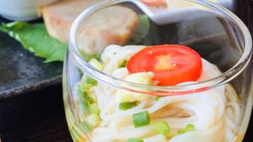 A clear glass bowl containing noodles, a slice of tomato, and chopped green onions.
