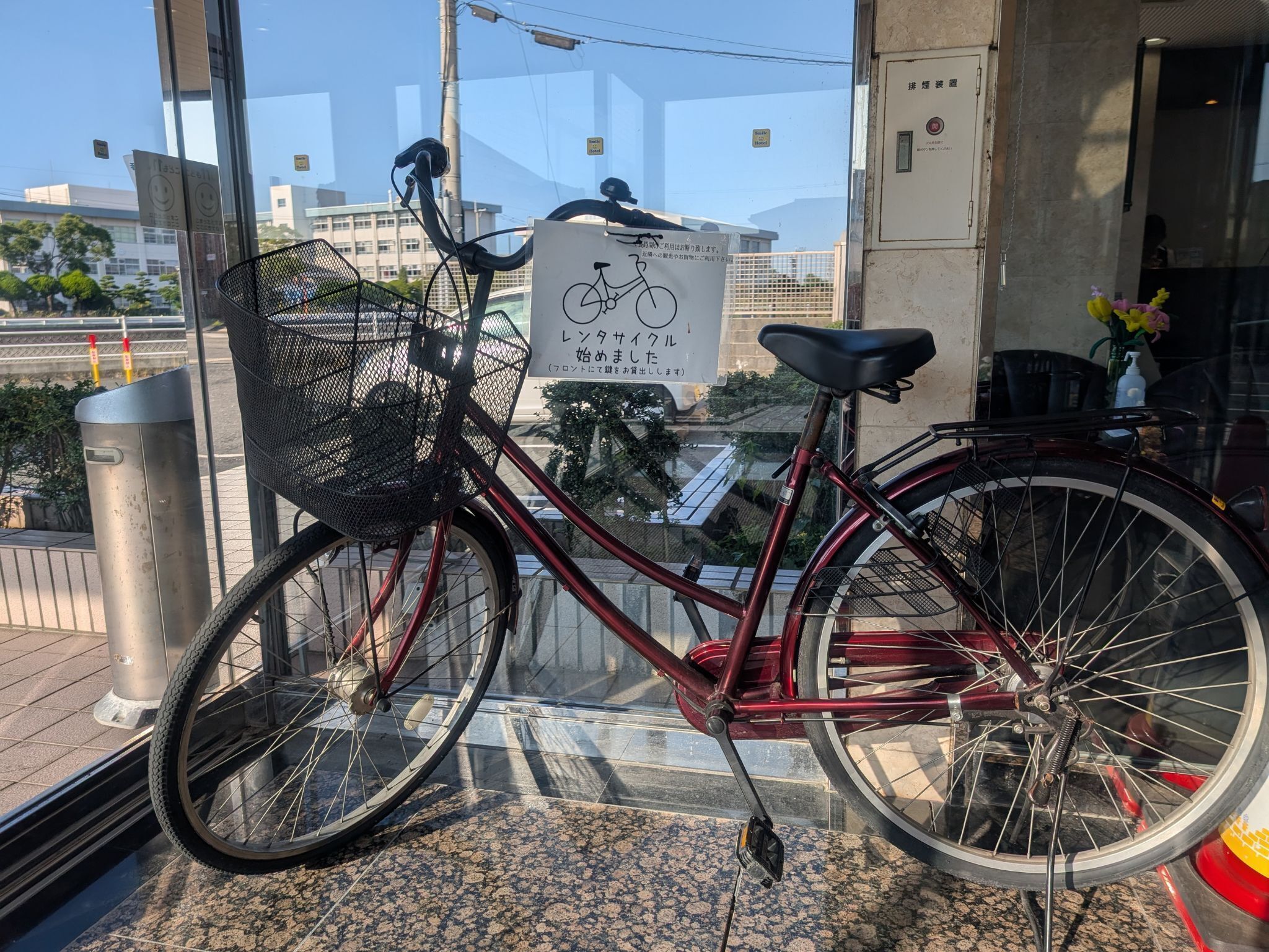A red bicycle with a basket and a sign in front of a building.