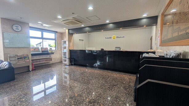 A reception area with a reception desk, a clock, and a wall-mounted sign that reads "Smile Hotel." - Smile Hotel FukuokaOkawa (Okawa)