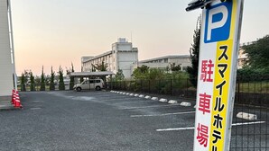 A parking lot with a white van, a building with a flat roof, and a sign with Japanese characters. - Smile Hotel FukuokaOkawa (Okawa)