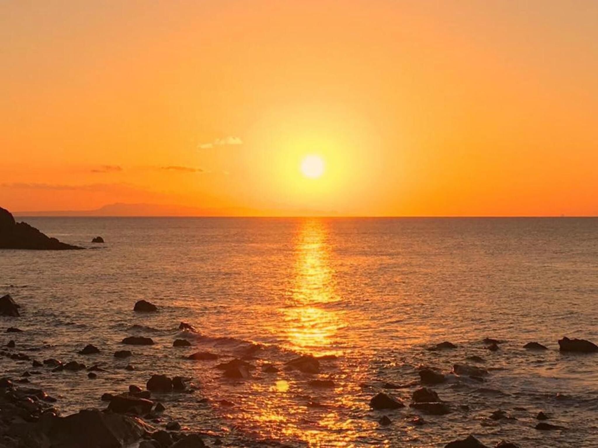 Un coucher de soleil sur une plage rocheuse, avec une eau calme qui reflète la lumière du soleil.