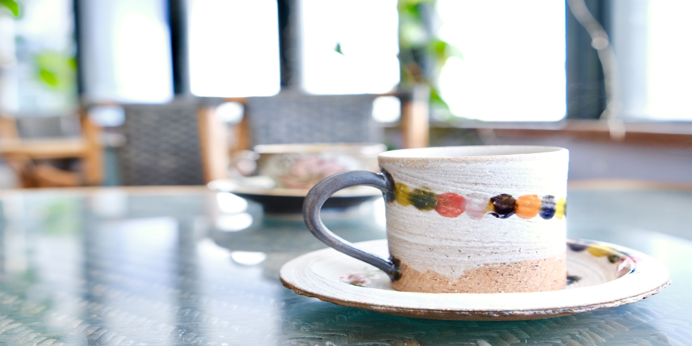 A ceramic mug with a colorful stripe on a saucer, placed on a glass table.
