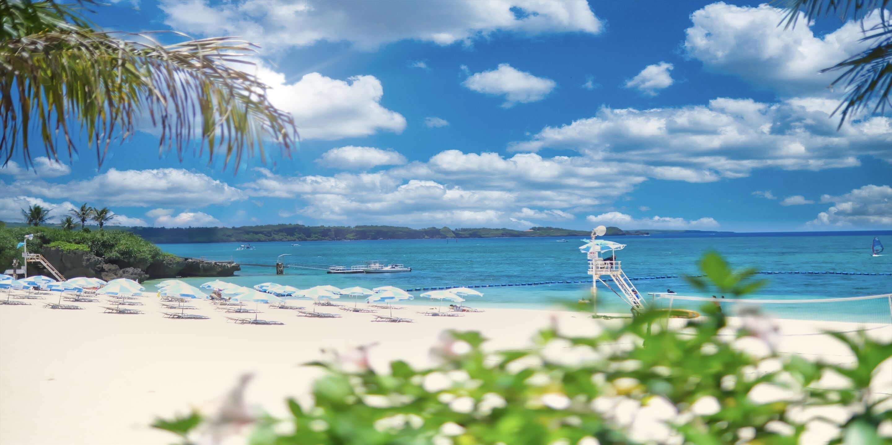 A beach with white sand, clear blue water, and a lifeguard tower.