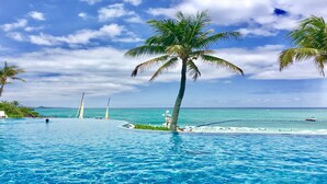 A pool with lounge chairs, palm trees, and a view of the ocean. - Pension Moon Villa (Onna)