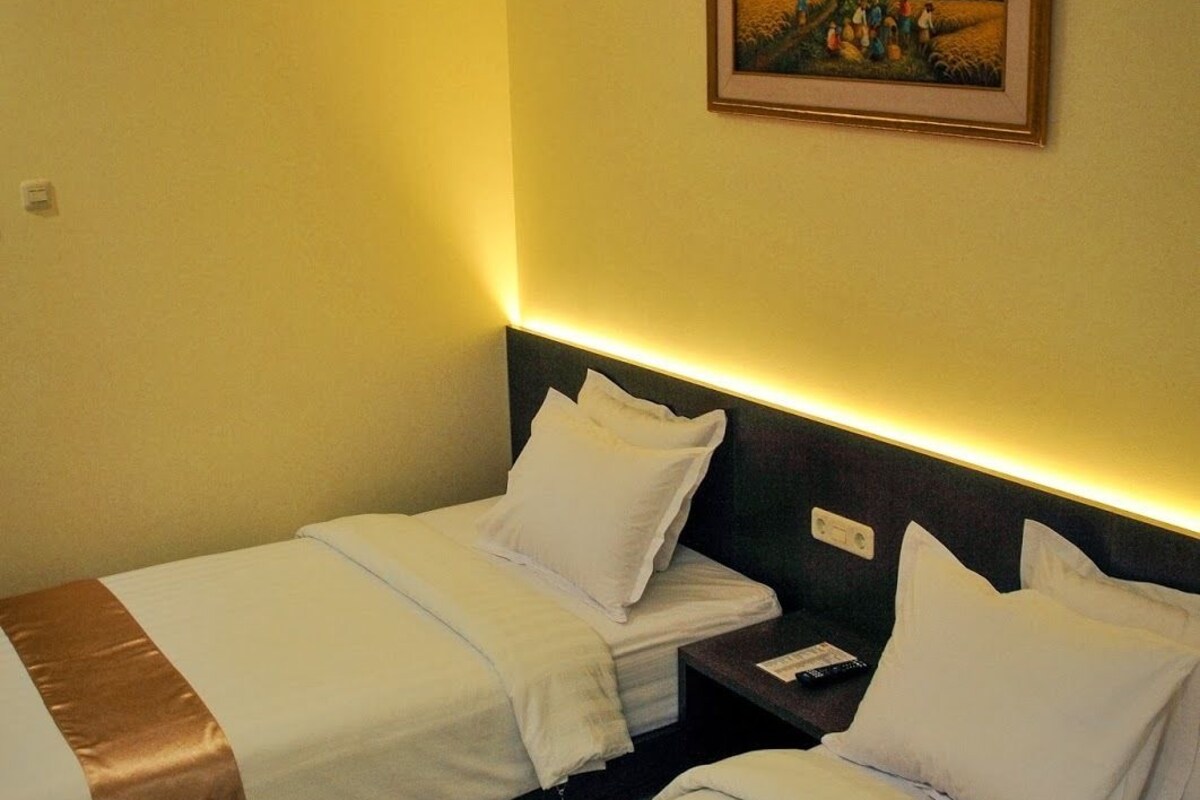 A hotel room with two beds, a nightstand, and a painting on the wall.