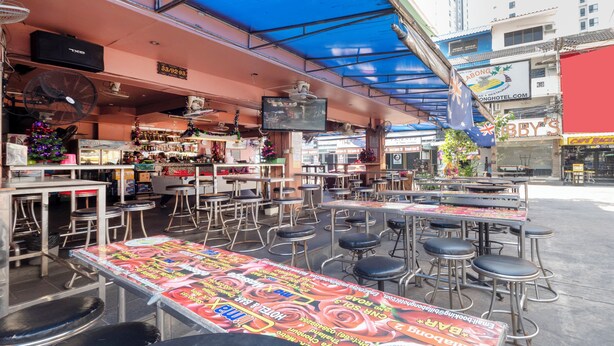 An outdoor bar area with tables and stools, a television screen, and a blue awning. - Billabong Hotel (Pattaya)