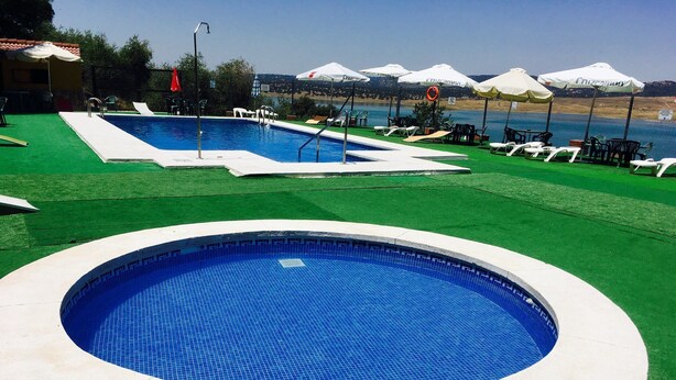 Une piscine entourée d’une terrasse, de chaises longues et de parasols.