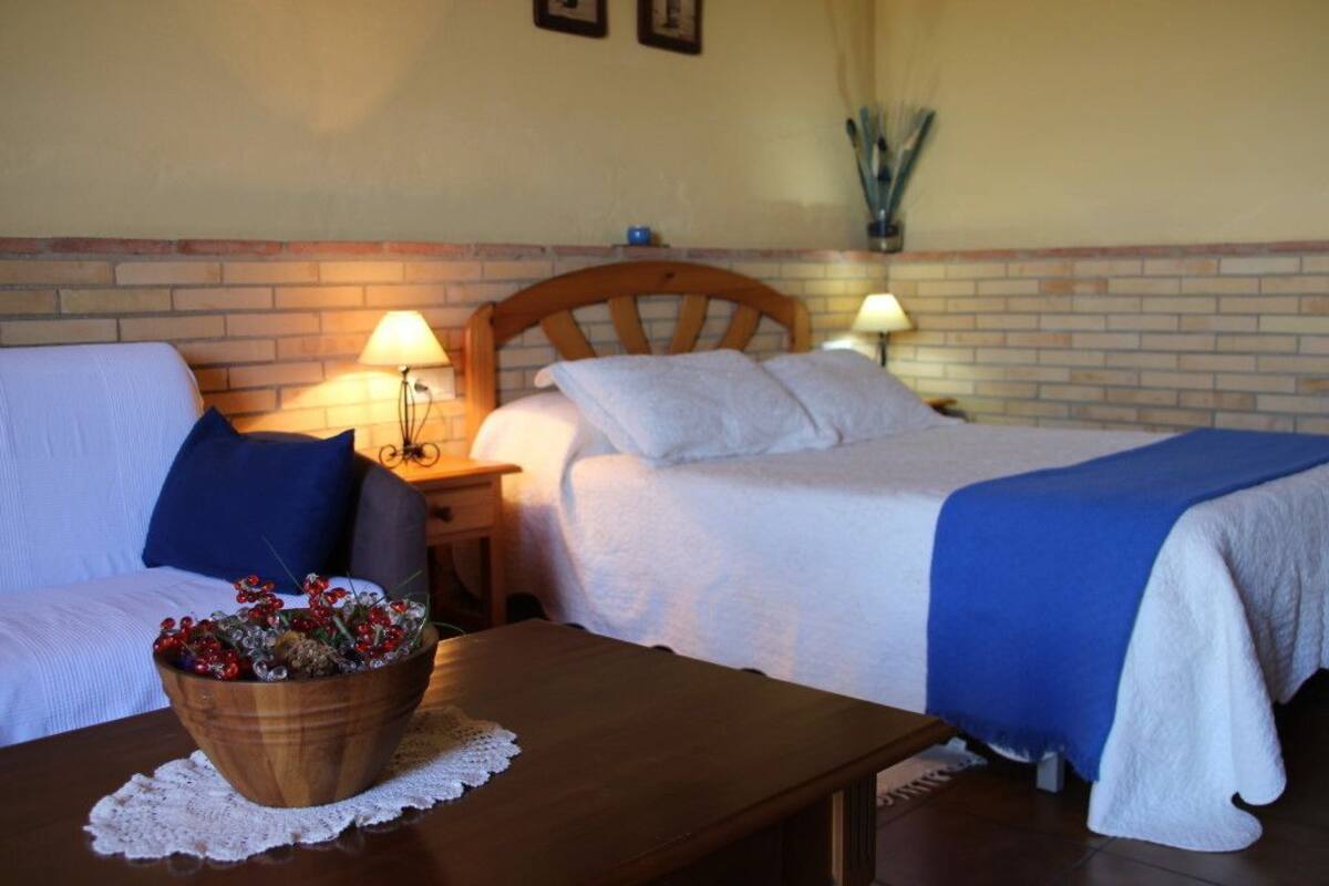 Een hotelkamer met twee bedden, een houten nachtkastje met lampen, een tafeltje met een fruitschaal, en een bakstenen muur.