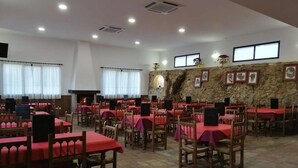 Un grand espace dédié à la salle à manger, avec plusieurs tables et chaises, un mur en pierre orné de tableaux encadrés et une cheminée.