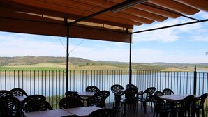 Une terrasse avec des tables et des chaises donnant sur un lac et des collines.
