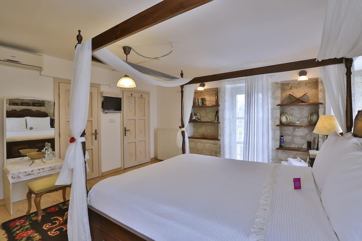 A hotel room with a large bed, a bedside table with a lamp, a wardrobe, and a small desk with a chair.