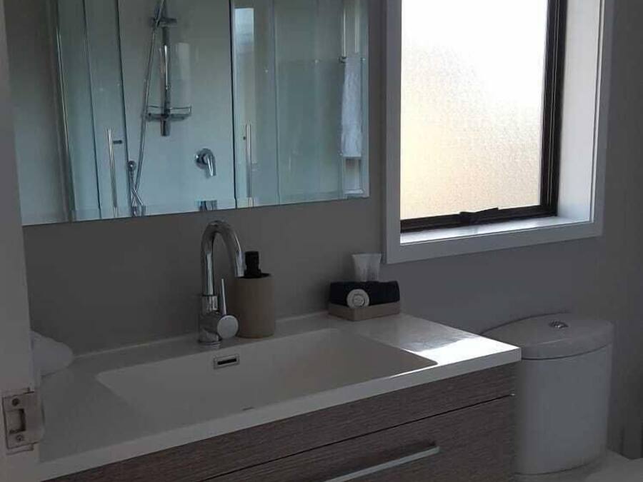Un baño con un espejo grande, un lavabo, un inodoro y una ventana.