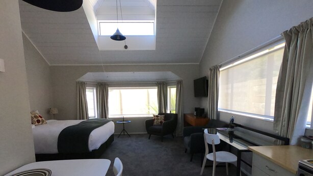 A hotel room with a bed, a desk, a chair, a small table, and a TV. - Ohakune Central Motels (Ohakune)