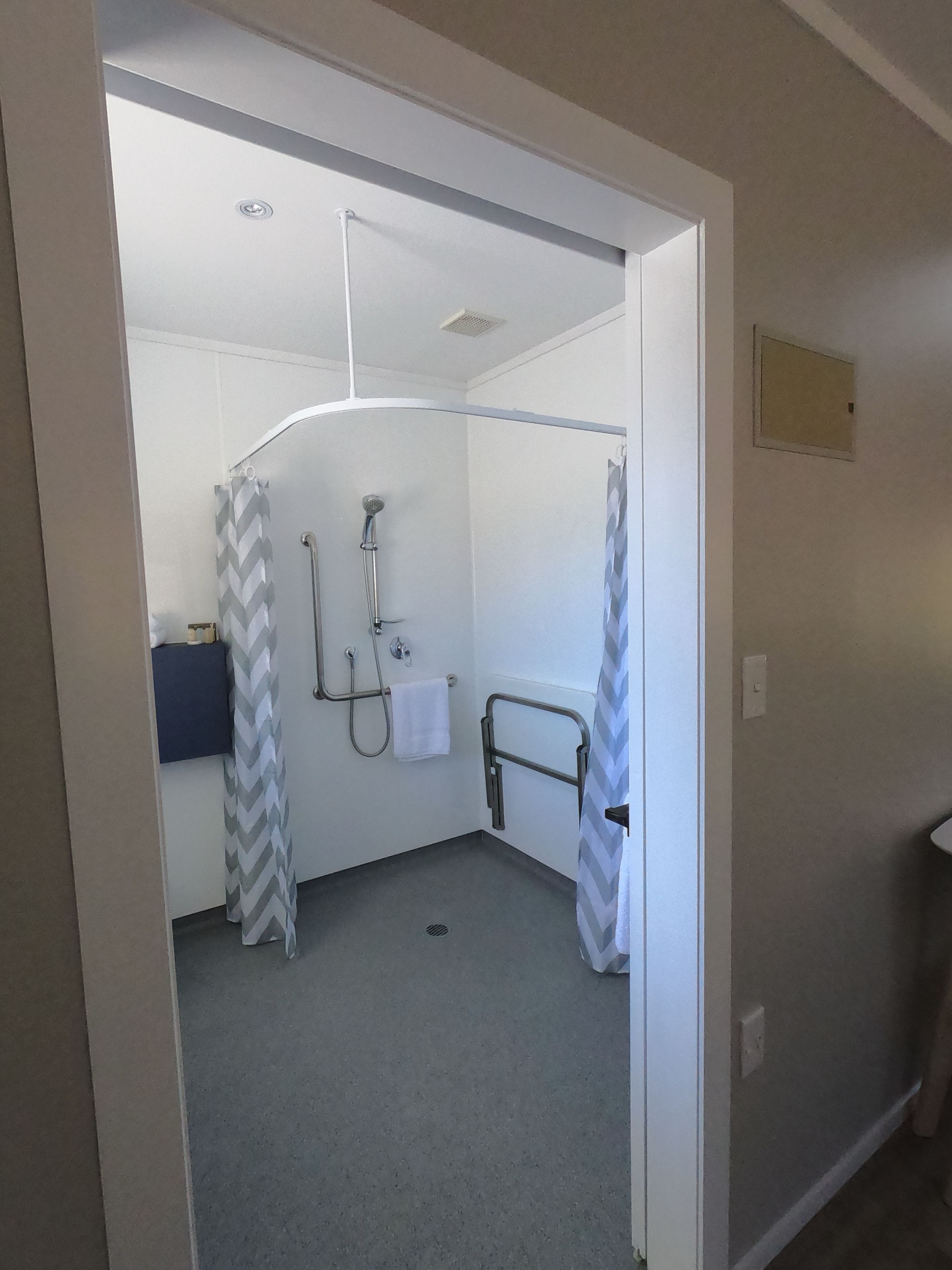 A small, enclosed shower area with a white shower curtain, a grab bar, and a towel rack.