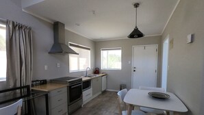 A compact kitchen with a stove, oven, and sink, a dining table with chairs, and a window providing natural light. - Ohakune Central Motels (Ohakune)