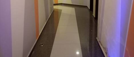 Un pasillo con suelo de baldosas, paredes blancas y una puerta al final.